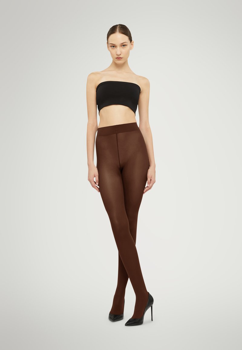 Bruna semi-opaka leggings med en slät textur, i kombination med en svart strapless-topp och högklackade skor, vilket skapar en smäcker silhuett.