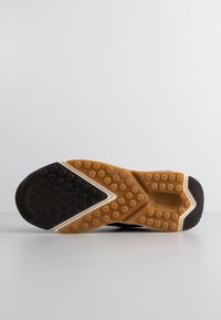Semelle de chaussure avec des sections en caoutchouc noir et marron présentant des grips circulaires et des motifs texturés pour une bonne adhérence sur surfaces lisses.