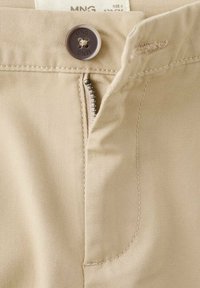 Bež hlače s sprednjim zadrgo in gumbom za zapenjanje. Tkanina je gladka na otip, z vidnimi šivi in detajlom žepa.