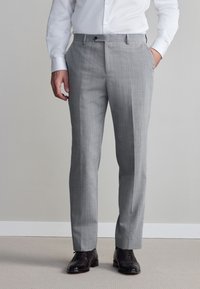 Pantaloni eleganti di colore grigio chiaro con trama, dal taglio sartoriale, dotati di tasche laterali e chiusura con un solo bottone, abbinati a scarpe eleganti nere.