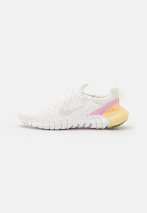 Biały but do biegania Nike z elastyczną, segmentowaną podeszwą, różowymi i żółtymi akcentami na pięcie oraz siateczkową cholewką zapewniającą oddychalność.