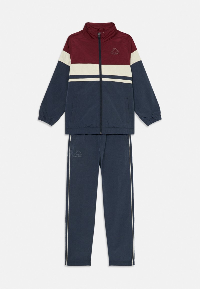 Treniņtērps ar bordo augšu, navy apakšu, ar baltām svītrām un logotipu. Izgatavots no viegla materiāla ar elastīgām aprocēm un jostasvietu.