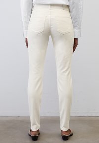 Jeans blancos ajustados con una textura suave, diseño de cinco bolsillos y detalles de costura sutiles, combinados con sandalias de tacón marrones.