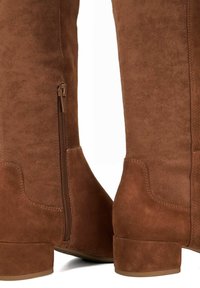 Brown suede knee-high boots featuring a side zipper, block heels, and smooth texture with visible stitching and seams.