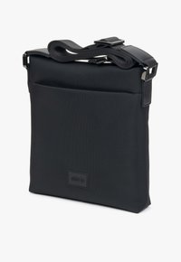 Czarna torba z teksturowanej tkaniny, o płaskim designie, z regulowanym paskiem, przednią kieszenią oraz skórzanymi detalami z embosowanym logo.