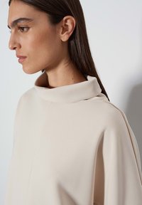 Beige top met een mock neck, een ontspannen pasvorm, zachte textuur en minimale details, met een licht gedrapeerd silhouet en een omgeslagen kraag.