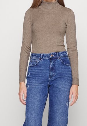 Bruine, geribde turtleneck trui met lange mouwen, gecombineerd met high-waisted blauwe denim jeans met beschadigde details en voorzakken.