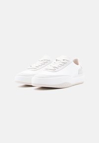 Λευκά αθλητικά παπούτσια με λείο συνθετικό επάνω μέρος, στρογγυλεμένη μύτη, δέσιμο με κορδόνια, υφασμένο λαστιχένιο πάτο και διακριτική λογότυπο στο πλάι.