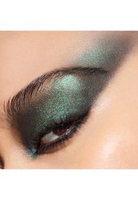 Close-up of an eye with dramatic dark green shimmer eyeshadow, blending into a soft black gradient, accentuated by defined eyelashes and brow.