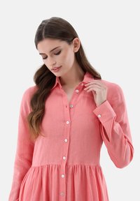 Rosa Leinenhemd mit Knopfleiste, langen Ärmeln und ausgestelltem Saum. Hat einen klassischen Kragen und Knöpfe entlang der Knopfleiste.