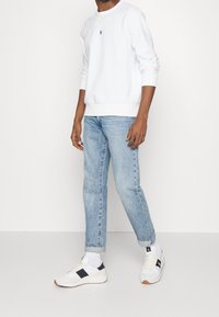 Biała bluza z okrągłym dekoltem, jasnoniebieskie jeansy o prostym kroju oraz białe trampki z granatowymi akcentami. Gładkie faktury, styl casualowy.