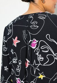 Schwarzer Stoff mit weißem Linienstil von Gesichtern und bunten Akzenten in Pink und Gelb. Das Design enthält einen subtilen Schlitz hinten.