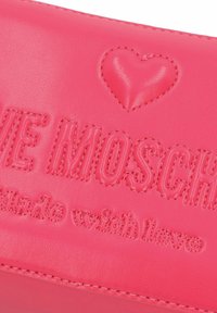 Borsetta in pelle rosa con testo in rilievo "LOVE MOSCHINO" e dettaglio a forma di cuore. Texture liscia con dettagli di cuciture a contrasto.