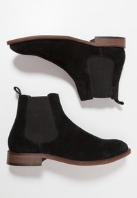 Bottes Chelsea en daim noir avec panneaux latéraux élastiques, bout arrondi, petit talon empilé et languette à l'arrière pour un enfilage facile.