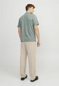 Šedé polokošile s krátkým rukávem, kombinované se svetle béžovými kalhotami s širokými nohavicemi a černými botami. Košile má postranní rozparky.