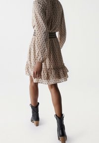 Hame dress beige, lyhythihainen, puffatut hihat, mustat geometriset kuviot, röyhelöhelma ja kireä vyötärö. Yhdistetty mustiin nilkkureihin.