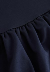 Laine navy dengan tekstur halus; dilengkapi dengan ruffle berkerut di bagian bawah, menciptakan volume dan dimensi. Bahan yang lembut dan ringan.