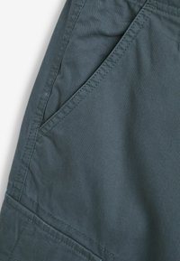 Dunkeltürkisfarbener Stoff von Shorts mit glatter Textur. Verfügt über eine Seiten Tasche, flache Nähte und ein schlichtes Design. Keine sichtbaren Muster oder Hardware.