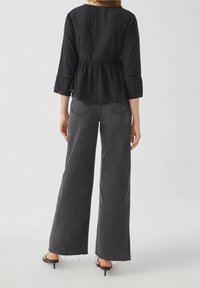 Top nero a pois con vita peplum e maniche a tre quarti, abbinato a jeans grigi a vita alta e gamba larga, e sandali neri con tacco.