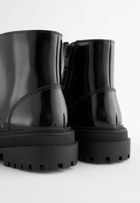 Stivaletti in pelle patinata nera con finitura liscia, puntetonde e suole in gomma spessa dotate di grip texture e cerniere laterali.