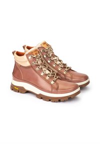 Botas de senderismo marrones con parte superior de cuero liso, detalles en beige, ojales metálicos y cordones. Suela gruesa de goma texturizada para tracción.