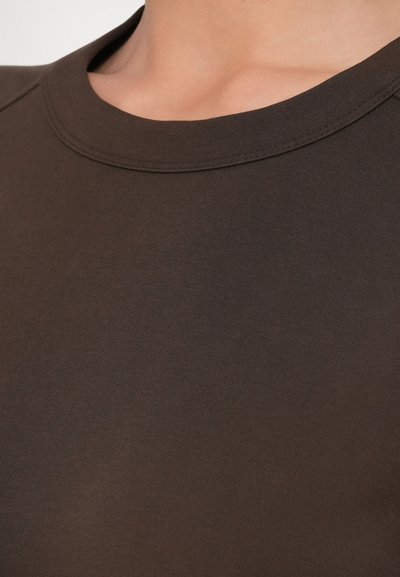 Κοντινό πλάνο ατόμου που φοράει σκούρο καφέ μπλουζάκι με στρογγυλή λαιμόκοψη, εμφανίζοντας το λαιμό και την ανώτερη περιοχή του στήθους.