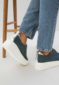 Schuhe mit einem Obermaterial aus dunkelblauem Leder, silbernen Absatzakzenten und einer weißen Plateau-Sohle, kombiniert mit taillierten blauen Jeans.