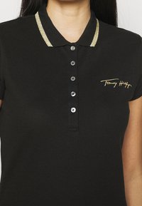 Sort polo t-shirt med en glitrende guldkrave, fem-knaps knaplukning og broderet guldlogo. Textureret stof med korte ærmer.