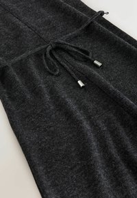 Graues Strickstoff-Kleidungsstück mit einer Kordelzug-Waiste und metallischen Enden. Weiche Textur mit einem subtilen Glanz. Lässiges Design mit lockerer Passform.