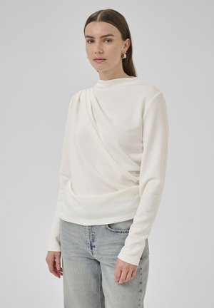 Crème top met lange mouwen en gedrapeerd voorkant ontwerp, zachte textuur, ronde hals en aansluitende mouwen, gecombineerd met lichtblauwe spijkerbroek.