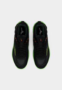 Ζευγάρι μαύρα και πράσινα αθλητικά παπούτσια με πορτοκαλί οφθαλμούς και λογότυπο, φαίνονται από πάνω σε λευκό φόντο.