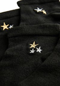 Schwarze Socken mit weicher Textur, die mit gestickten Sternen in Gold, Hellblau und Weiß versehen sind. Eine Nahaufnahme hebt die Nähdetails hervor.
