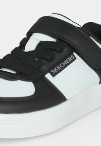 Ασπρόμαυρο αθλητικό παπούτσι Skechers με κορδόνια και βέλκρο σε λευκό φόντο.