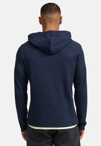 Sudadera con capucha de color navy con un diseño texturizado y canalé. Mangas largas y un dobladillo bajo, con una capucha sin herrajes visibles.
