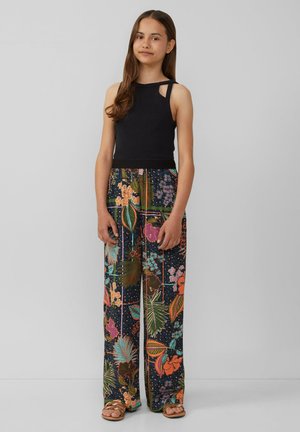 Haut sans manches noir avec découpes aux épaules, associé à un pantalon large arborant un motif floral et feuillu coloré sur un fond sombre.