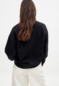 Czarna, oversize bluza z opadającymi ramionami, prążkowanymi mankietami i pasem. Noszona z luźnymi, białymi spodniami.