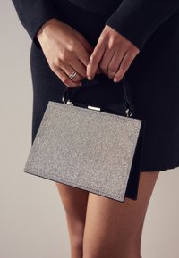 Melna rokassoma ar taisnstūrveida formu, rotāta ar sudraba rhinestones, ar augšējo rokturi un spīdīgu sudraba aizdari.