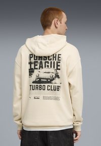 Felpa crema con cappuccio, caratterizzata da una stampa grafica nera vintage sul retro che recita "Porsche League Turbo Club". Tessuto in cotone misto testurizzato.