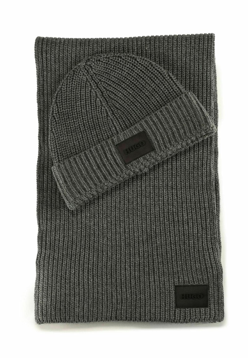 Bufanda de punto acanalado gris oscuro y gorro a juego, ambos con parches rectangulares negros de la marca Hugo.