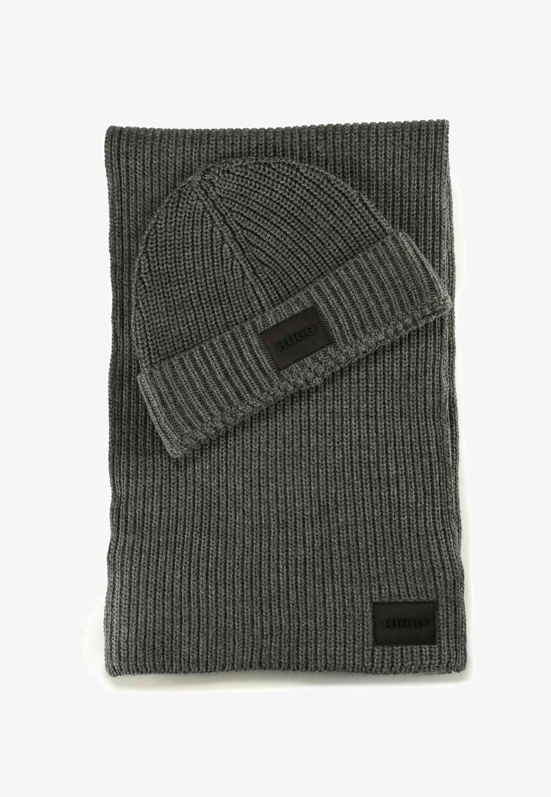 Bufanda de punto acanalado gris oscuro y gorro a juego, ambos con parches rectangulares negros de la marca Hugo.