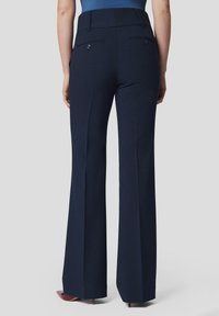 Granatowe spodnie o szerokim kroju, gładkim materiale, tylnych kieszeniach z zapięciem na guziki oraz dopasowanej talii.