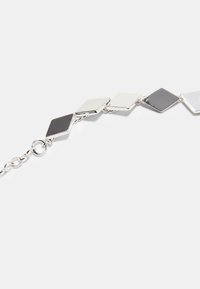 Bracelet en argent avec des maillons en forme de losange alternant noir et blanc, surface texturée et connexions en chaîne circulaire.