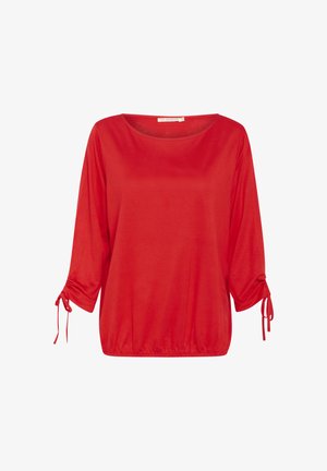 Raudona, laisvai krentanti tunika su apvali iškirpte, trimis ketvirtadaliais rankovėmis ir virvutėmis ant rankogalių. Minkšta tekstūra, kasdieniškas dizainas.