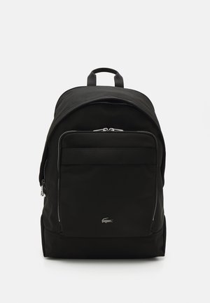 Sac à dos noir en tissu durable ; présente une forme arrondie, une poche zippée à l'avant, des accents argentés et un logo en bas à l'avant.