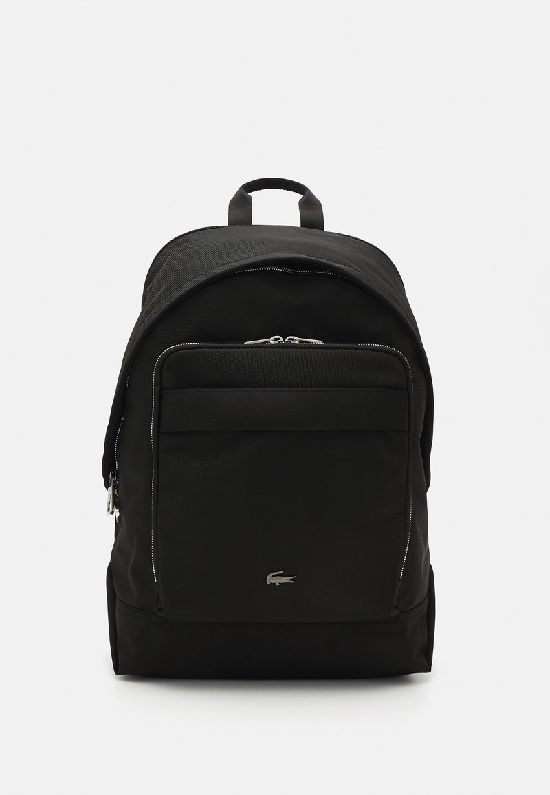 Sac à dos noir en tissu durable ; présente une forme arrondie, une poche zippée à l'avant, des accents argentés et un logo en bas à l'avant.
