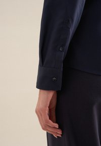 Marineblauwe langermige shirt met knoopmanchetten en gedetailleerde stitching. Glad, stoffen textuur met een getailleerde pasvorm zichtbaar bij de pols.