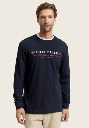 Marineblauwe T-shirt met lange mouwen, voorzien van een ronde hals, witte en rode bedrukte tekst en een casual pasvorm. De stof is glad en licht rekbaar.