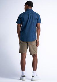 Korte mouwen donkerblauwe shirt met een button-down kraag, gecombineerd met kaki shorts. Bevat twee achterzakken en witte sokken met sneakers.