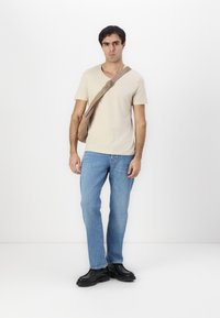 Beige kurzärmliges T-Shirt, hellblaue Jeans, schwarze klobige Schuhe mit dicker Sohle und eine tanfarbene Umhängetasche mit verstellbarem Riemen.