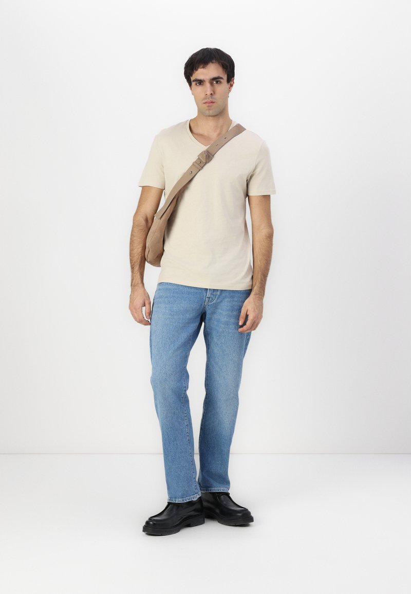 Beige kurzärmliges T-Shirt, hellblaue Jeans, schwarze klobige Schuhe mit dicker Sohle und eine tanfarbene Umhängetasche mit verstellbarem Riemen.